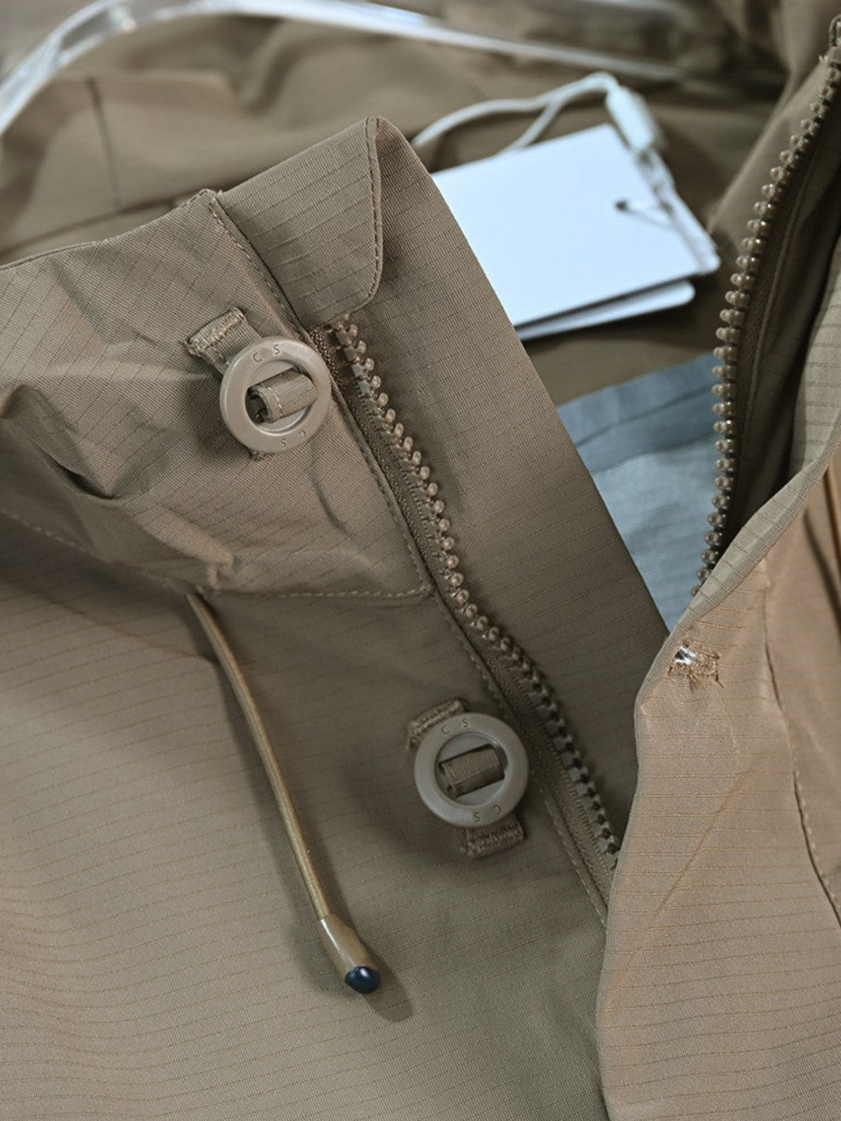 By Old Money beige water-repellent hooded jacket featuring a zip closure, snap buttons, and drawstring hood.