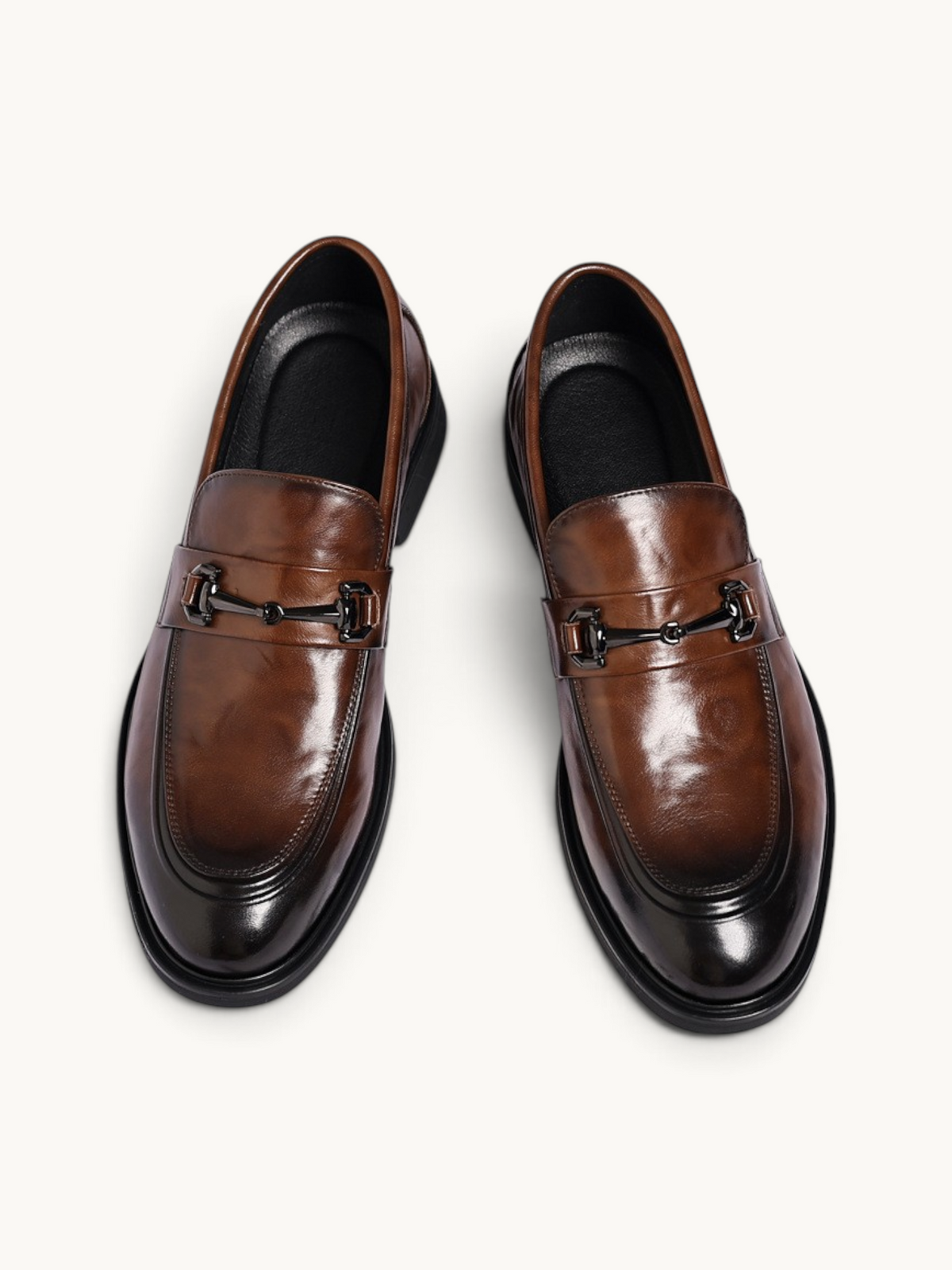 By Old Money brown leather loafers with a polished finish, metal horsebit detail, and rounded toe, top-down view.
