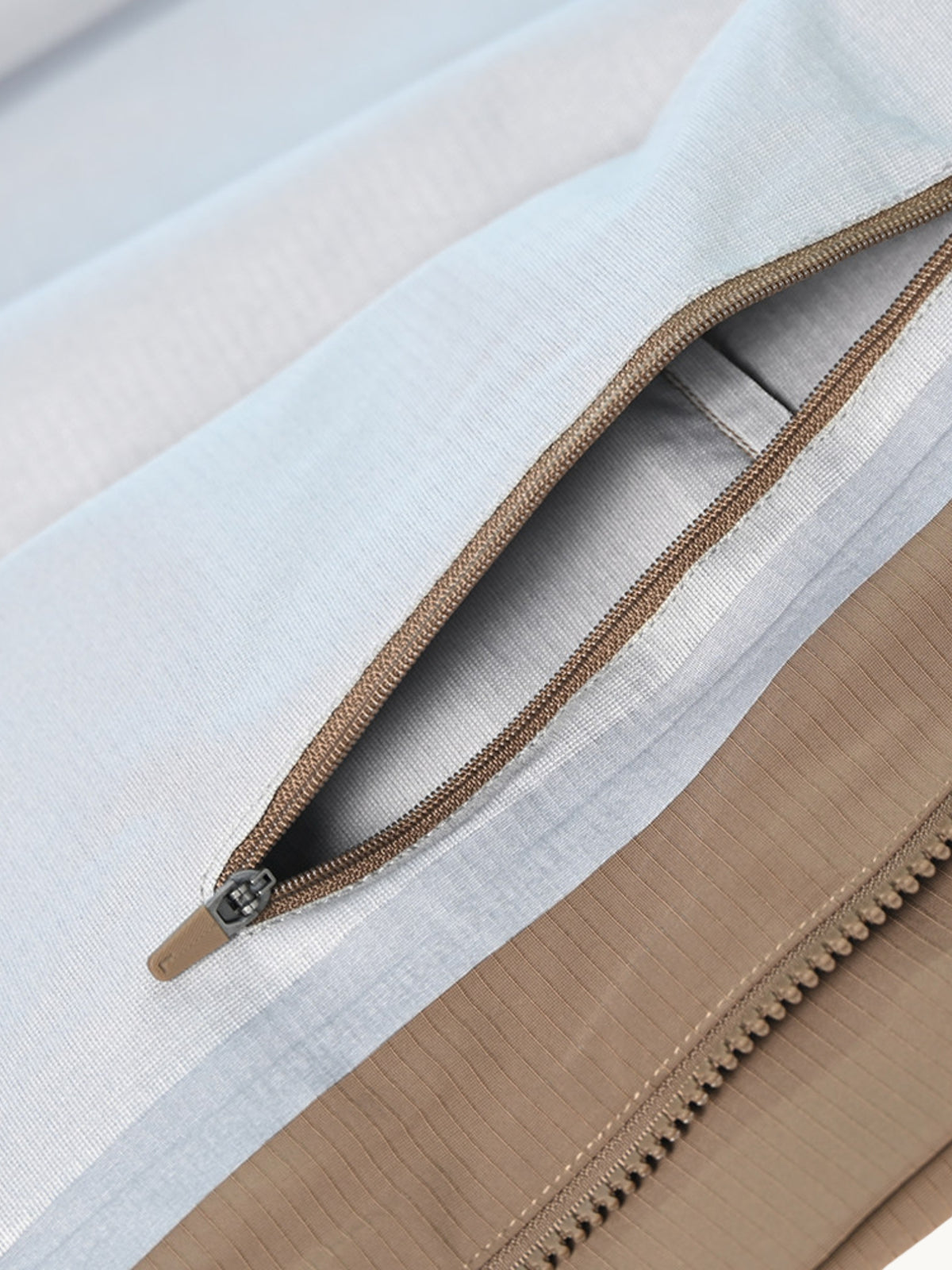Detail d'une poche zippee sur tissu bleu clair, panneau beige et fermeture marron