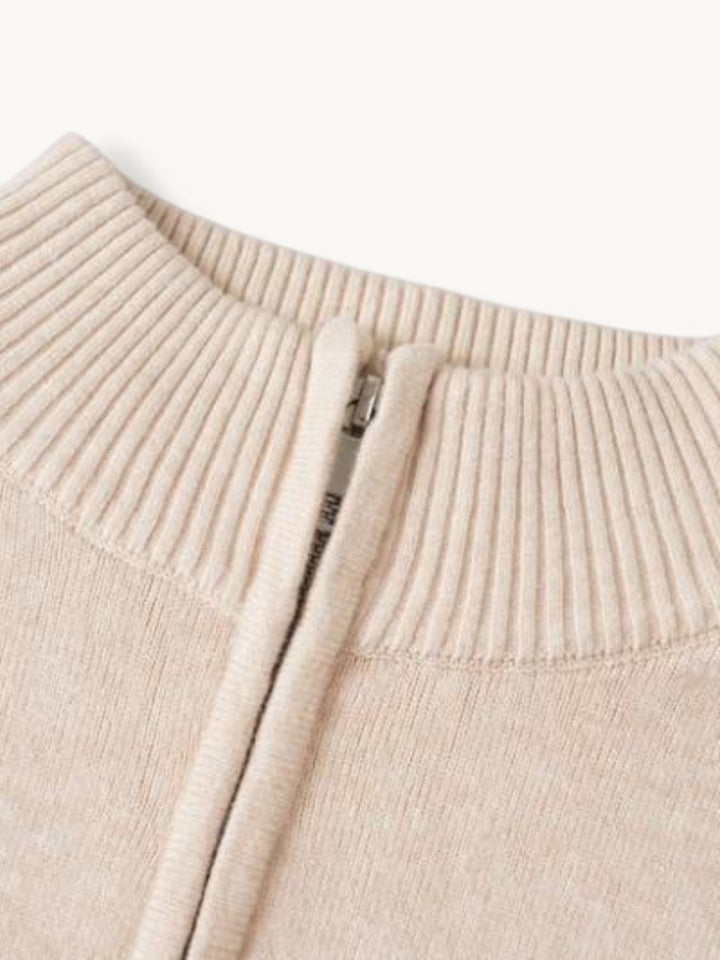 Détail du col zippé d'un pull en maille beige, bord côtes et curseur métallique