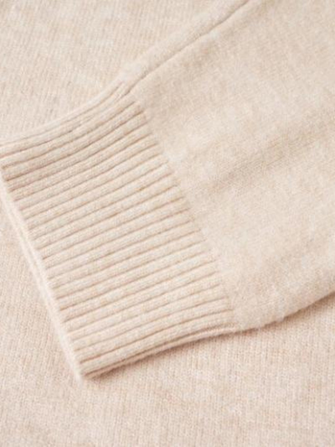 Gros plan sur la manche et le poignet côtelé du pull en maille beige