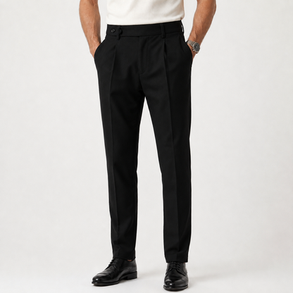 Black tapered trousers with pleats and belt loops, worn by model with cream shirt