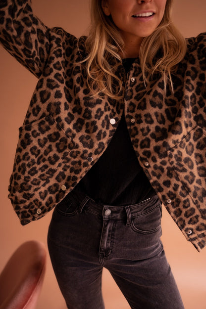 Blouson imprimé léopard ouvert, bras levés, porté avec un jean gris