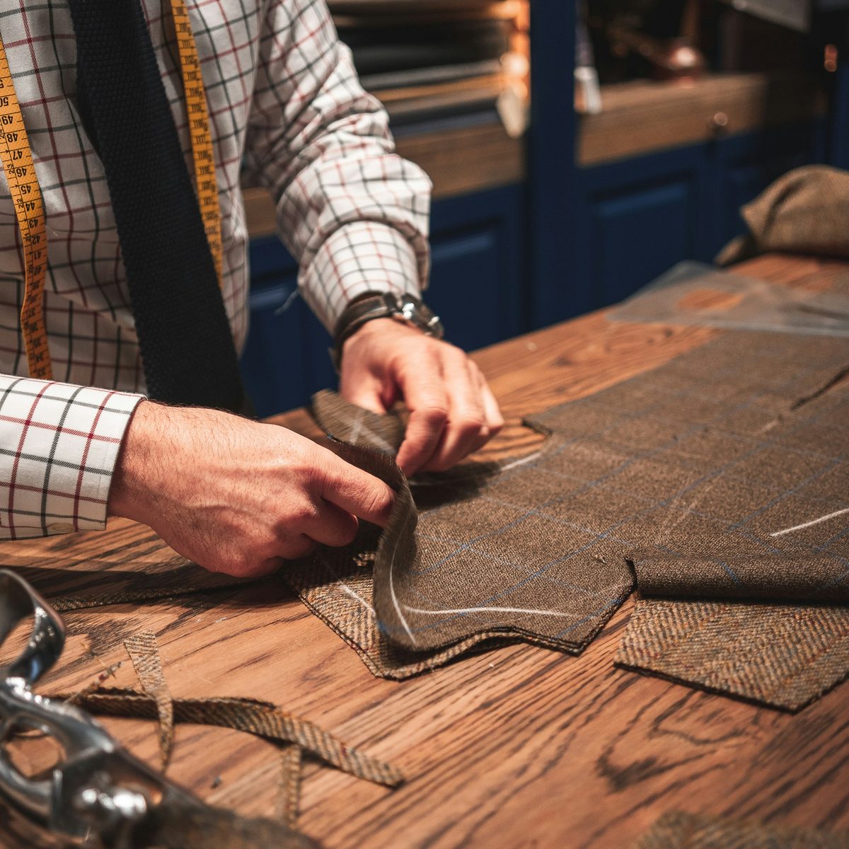 Tailleur découpant un tissu de laine à la main sur une table d'atelier