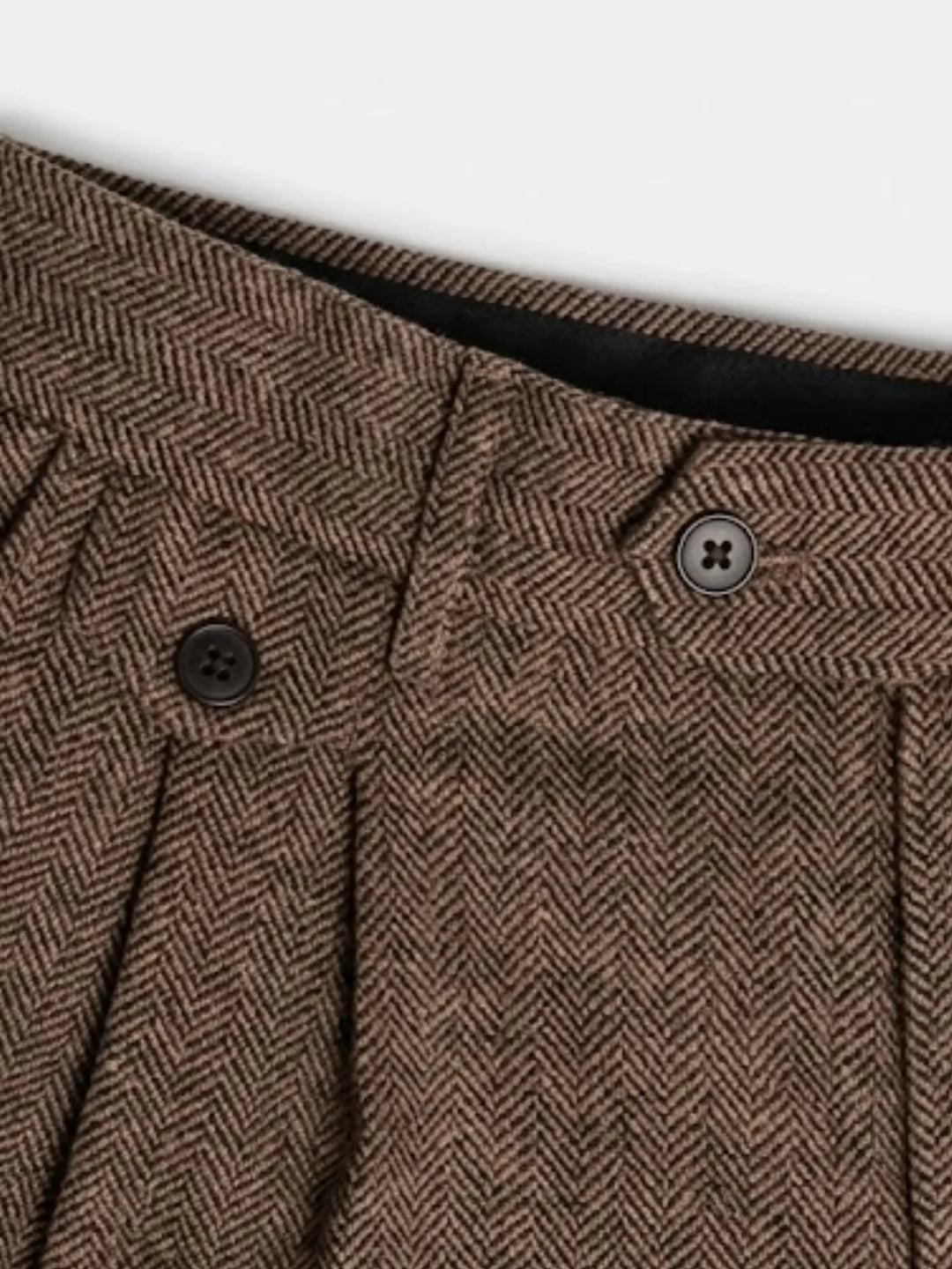 Gros plan sur la taille boutonnée d'un pantalon à plis en chevrons bruns