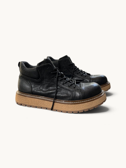 By Old Money black full-grain leather work boots with a thick lugged tan sole and mid-height ankle support.