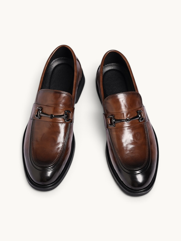 By Old Money brown leather loafers with a polished finish, metal horsebit detail, and rounded toe, top-down view.