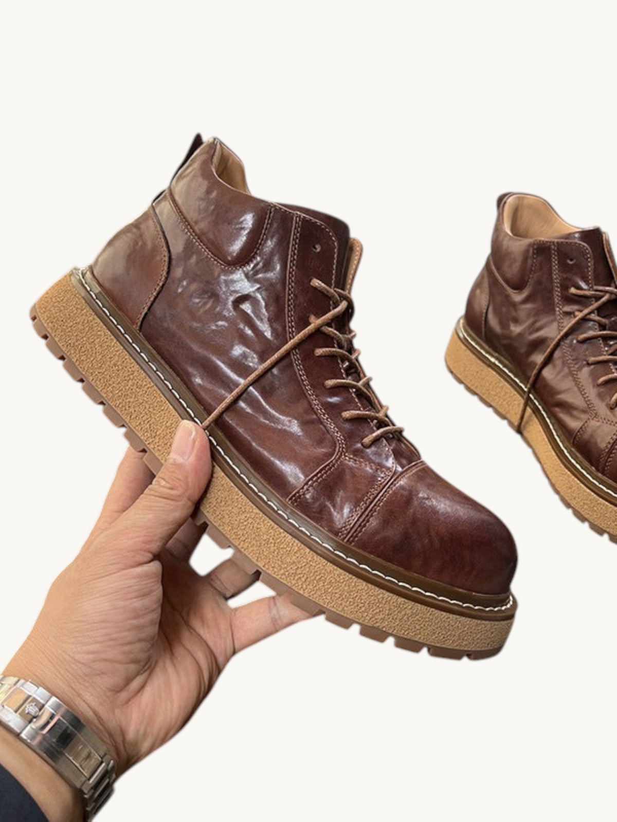 By Old Money brown full-grain leather work boots with a thick lug sole and lace-up design held in a hand