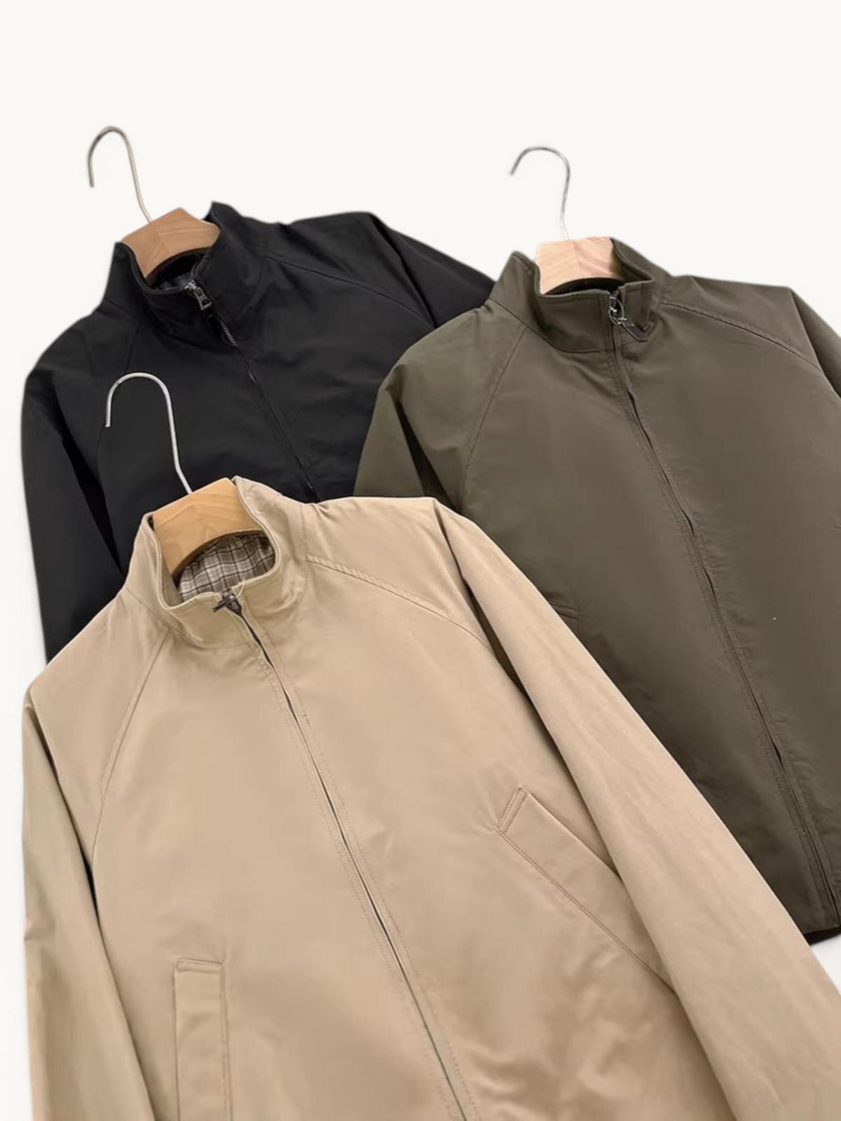 By Old Money lightweight zip-up jackets with stand collars in black, olive green, and beige on wooden hangers