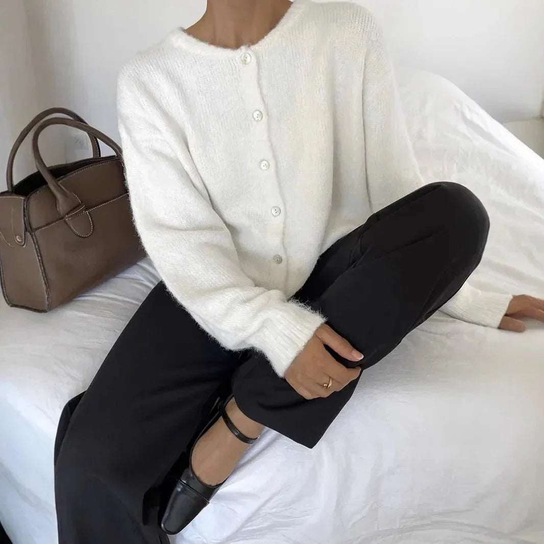 Cardigan boutonné blanc à col rond, porté assis avec un pantalon noir