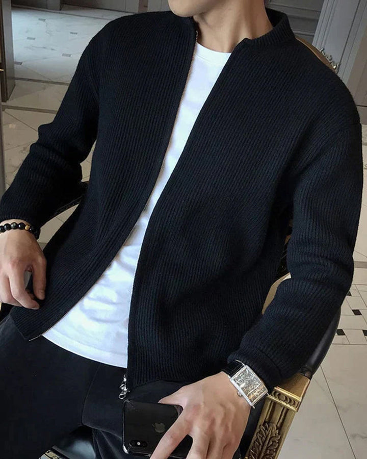Cardigan zippé noir en maille côtelée porté ouvert sur un t-shirt blanc et un pantalon foncé