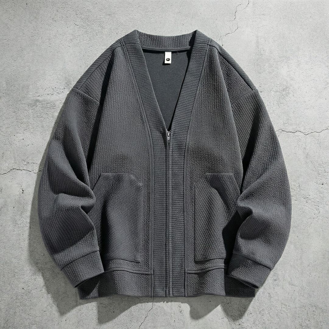 Cardigan zippé gris à col V posé sur du béton, deux poches et poignets côtelés