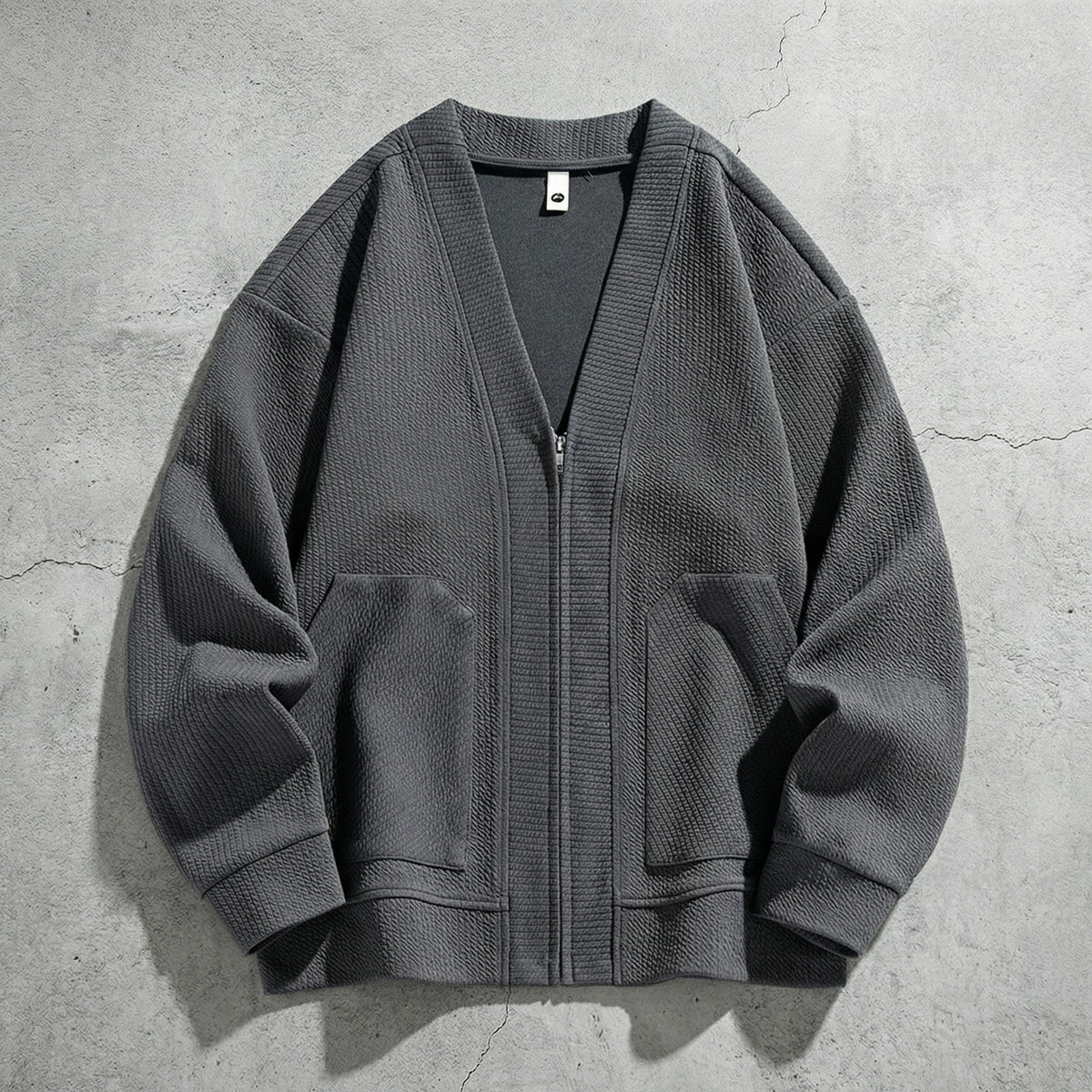 Cardigan zippé gris à col V posé sur du béton, deux poches et poignets côtelés