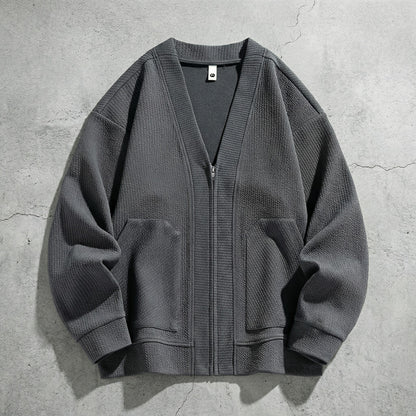 Cardigan zippé gris à col V posé sur du béton, deux poches et poignets côtelés