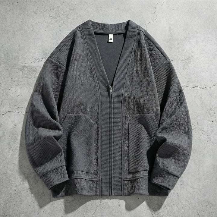 Cardigan zippé gris à col V posé sur du béton, deux poches et poignets côtelés