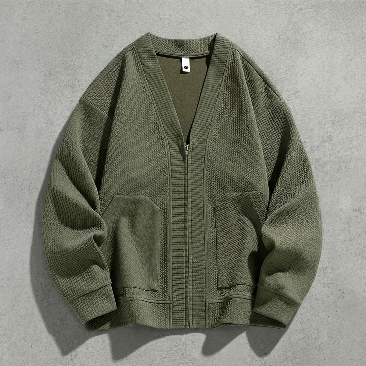 Cardigan zippé vert kaki à col V à plat sur du béton, maille gaufrée et poches basses
