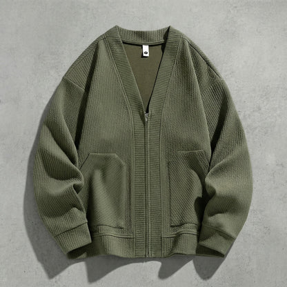 Cardigan zippé vert kaki à col V à plat sur du béton, maille gaufrée et poches basses