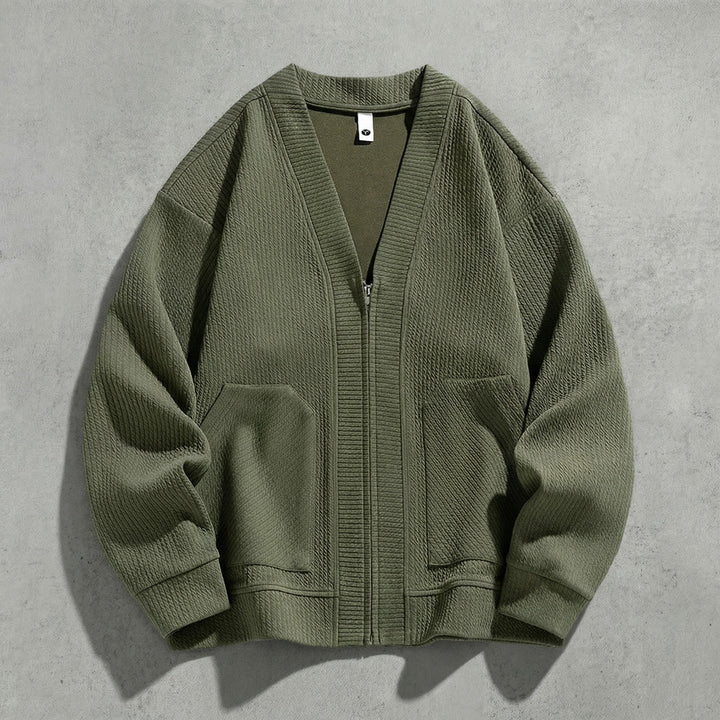Cardigan zippé vert kaki à col V à plat sur du béton, maille gaufrée et poches basses