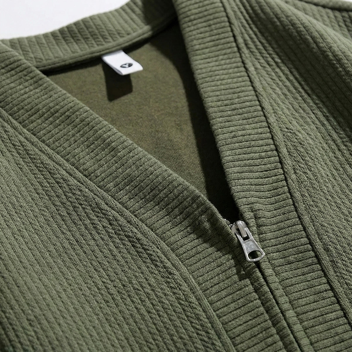 Gros plan sur le col V vert kaki, le curseur du zip et l'étiquette blanche cousue