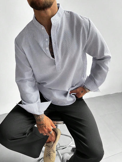 Homme assis en chemise à fines rayures grises, col mao ouvert et pantalon noir