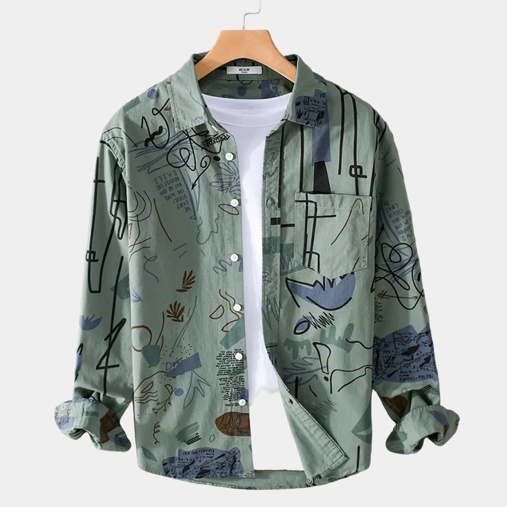 Chemise vert sauge à motifs abstraits, ouverte sur un t-shirt blanc, sur cintre en bois