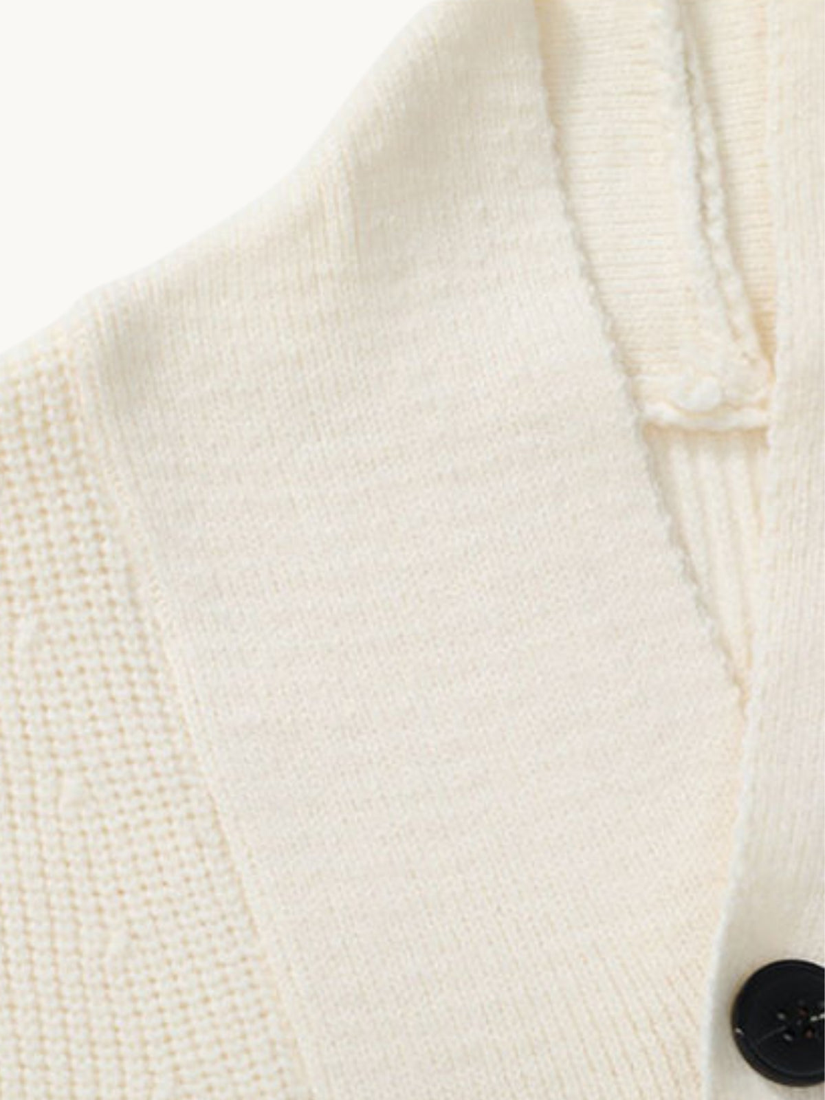 Gros plan sur le col en maille écrue du cardigan et son bouton noir