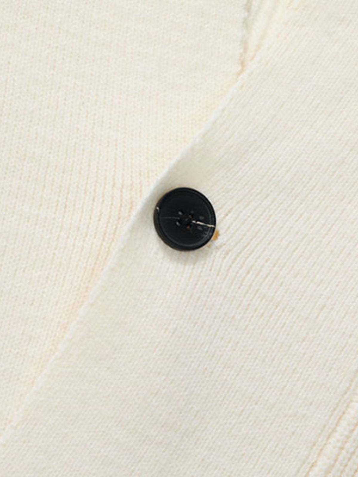 Gros plan sur un bouton noir et la maille écrue du cardigan