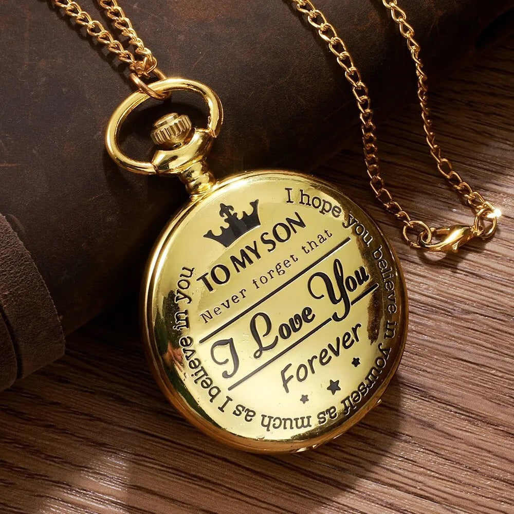 Montre de poche dorée fermée, couvercle gravé d'un message, chaîne posée sur un fond en bois
