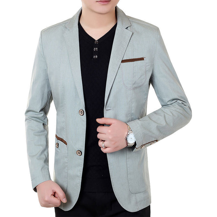 Blazer gris vert à passepoil marron sur les poches, porté sur un haut noir à col V
