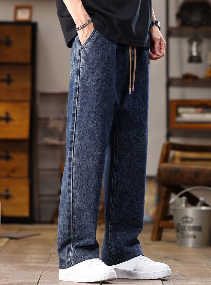 Jean bleu foncé de profil, main dans la poche, cordon de serrage qui pend à la taille
