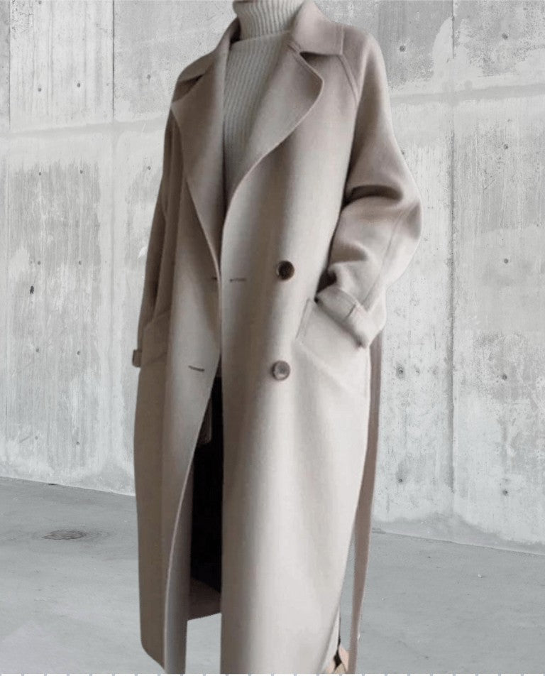 Manteau long en laine beige porté ouvert devant un mur en béton