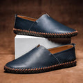 Paire de mocassins homme bleu marine à couture sellier, posée sur un socle blanc