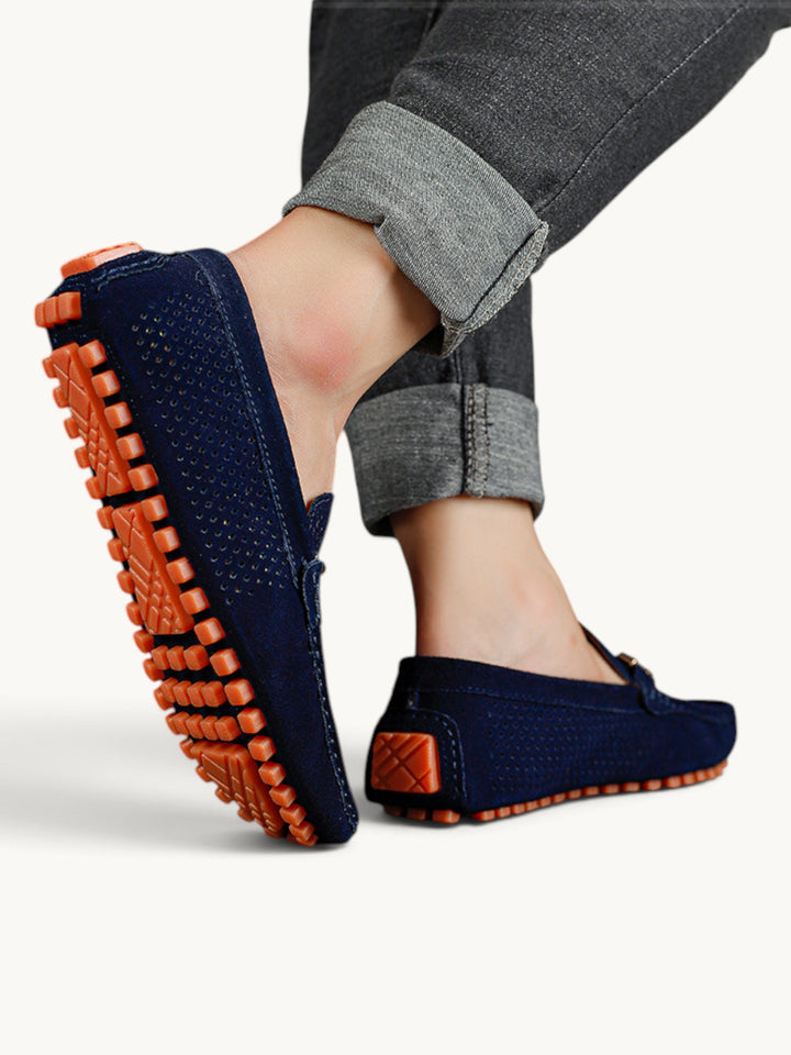 Mocassins bleu marine en cuir perforé portés, semelle à picots orange visible