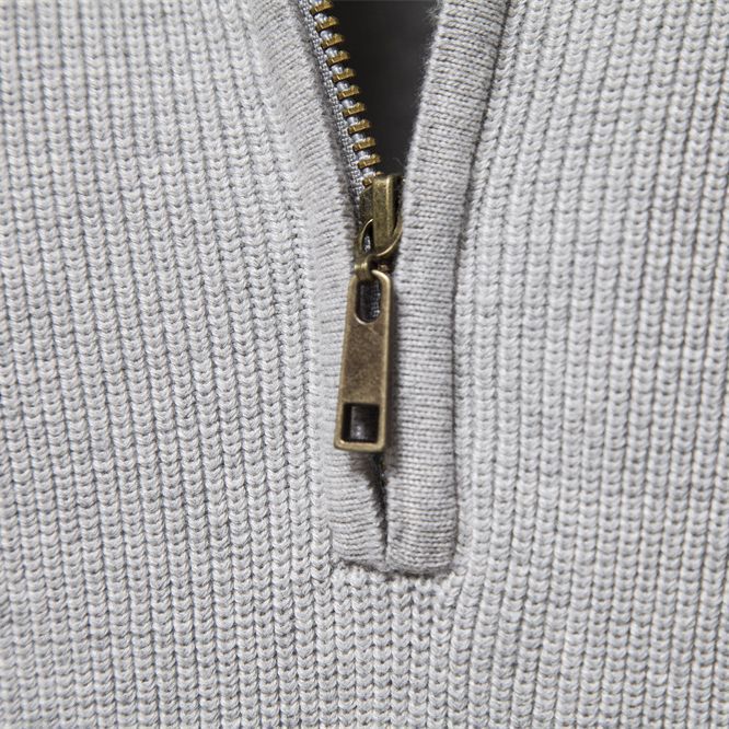 Gros plan sur le col côtelé gris et le curseur de zip en laiton du pull