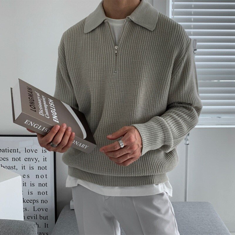 Pull col polo en maille côtelée gris porté par un homme, livre en main