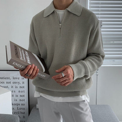 Pull col polo en maille côtelée gris porté par un homme, livre en main
