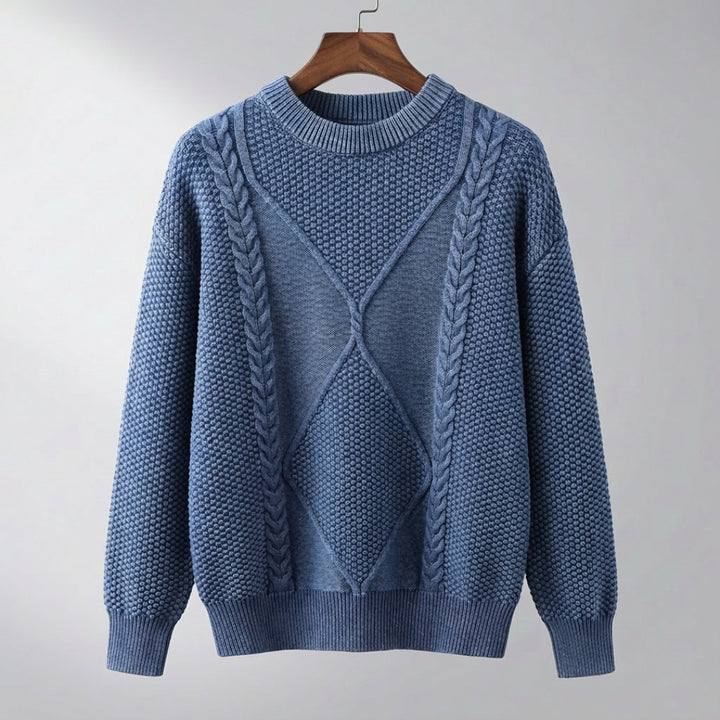 Pull bleu jean à col rond, torsades et losange en relief, suspendu à un cintre en bois