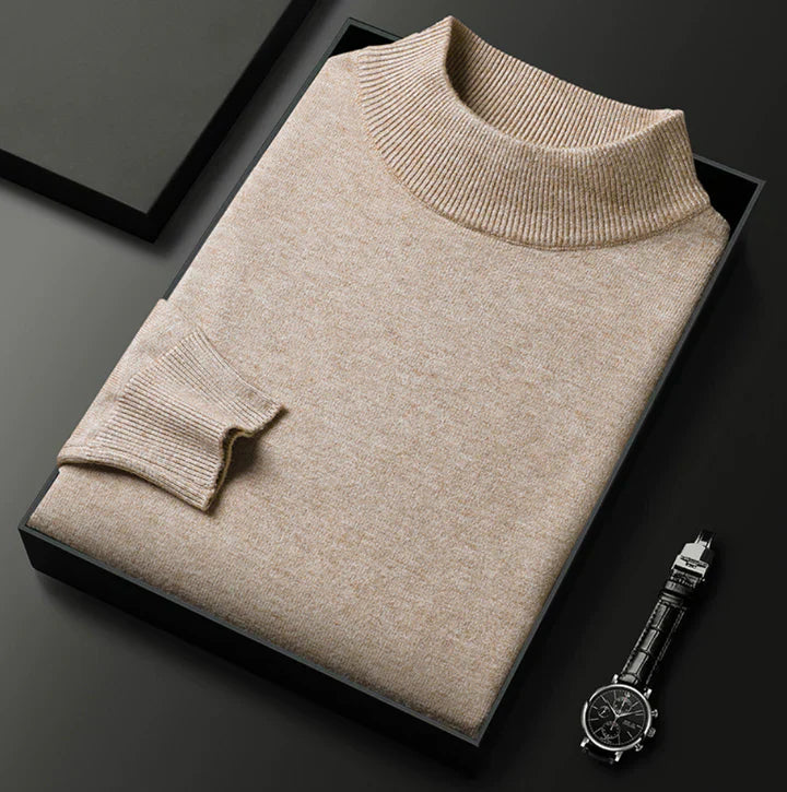 Pull beige chiné à col montant, plié dans un coffret noir à côté d'une montre