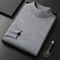 Pull gris clair chiné à col montant, plié dans un coffret noir à côté d'une montre