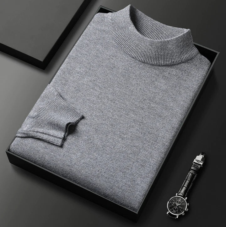 Pull gris clair chiné à col montant, plié dans un coffret noir à côté d'une montre
