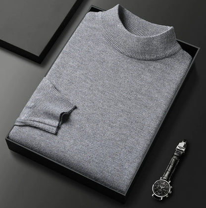 Pull gris clair chiné à col montant, plié dans un coffret noir à côté d'une montre
