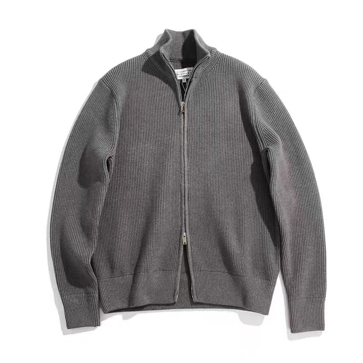 Cardigan gris en maille côtelée à col montant et double zip, posé à plat sur fond blanc