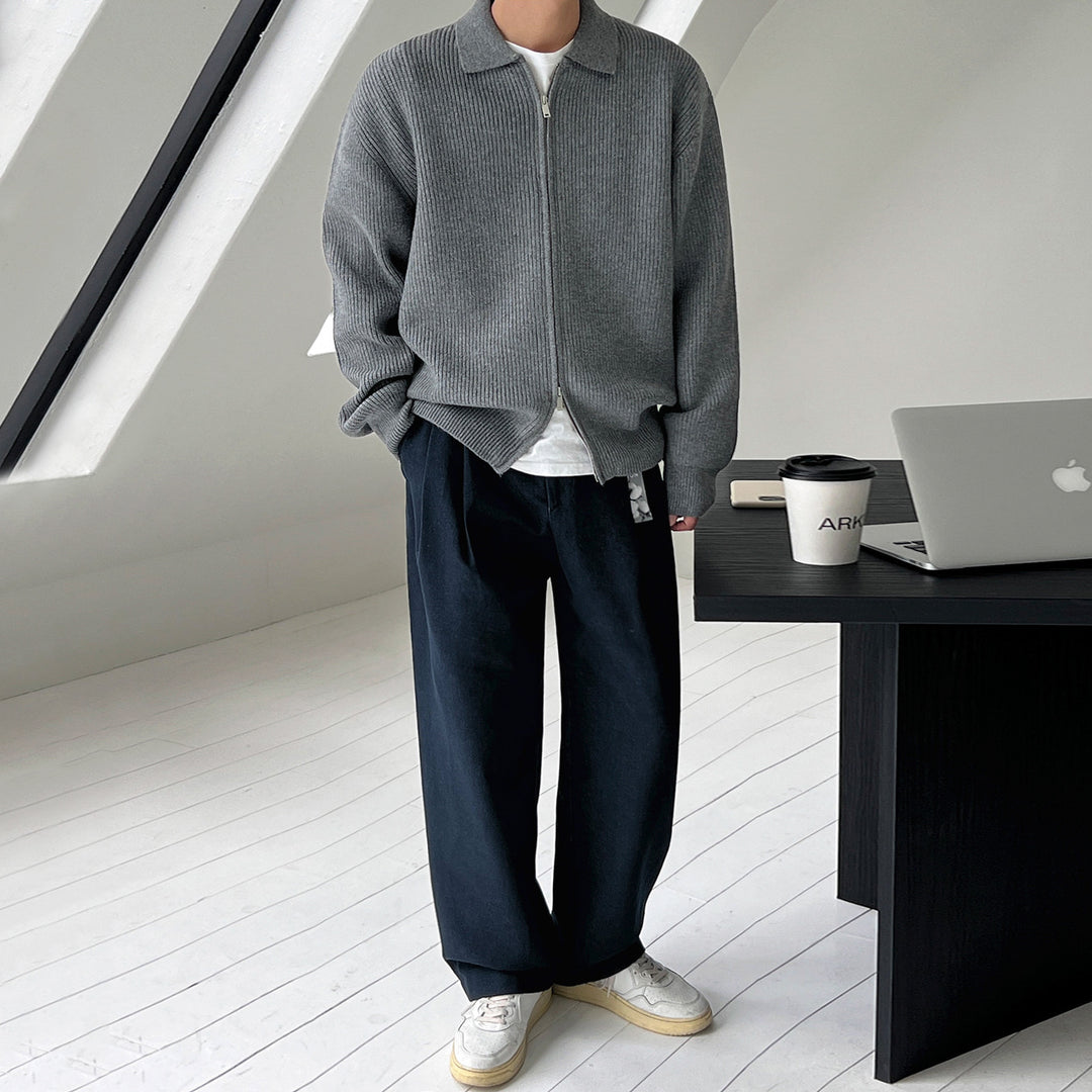 Homme portant une veste en maille côtelée grise à col chemise et zip, avec un pantalon large noir