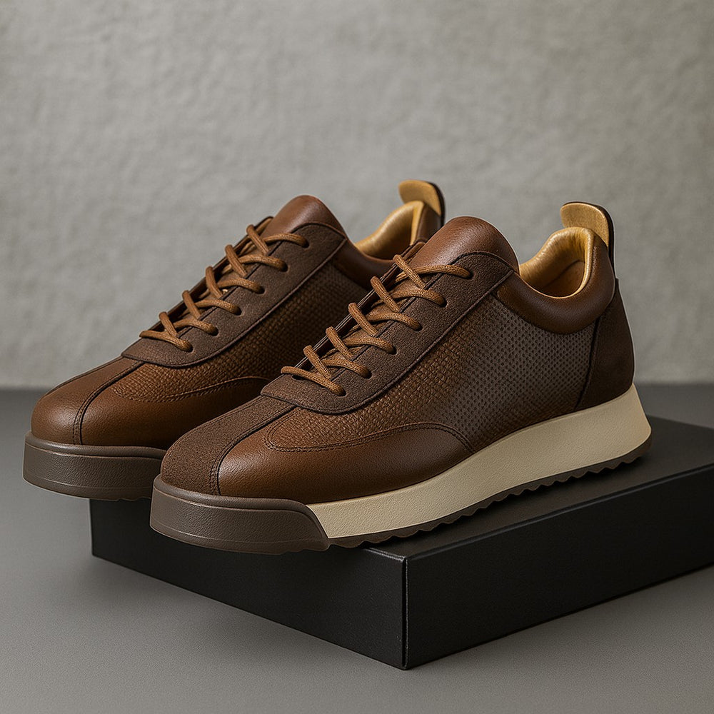 Paire de sneakers marron posées sur une boîte noire devant un mur texturé