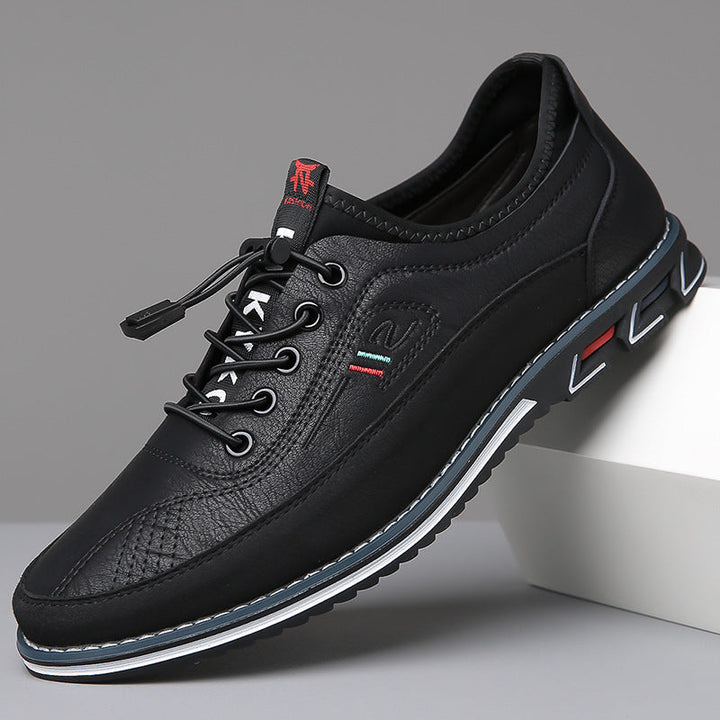 Sneaker basse en cuir noir appuyée sur un socle blanc, liseré bleu et blanc