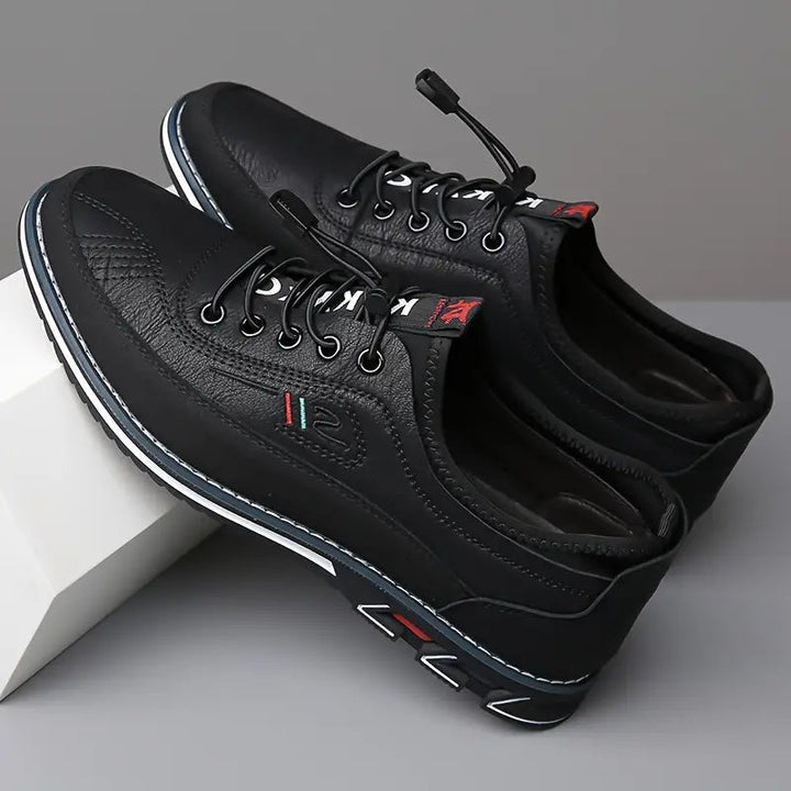 Paire de sneakers en cuir noir en appui sur un socle blanc, lacets élastiques