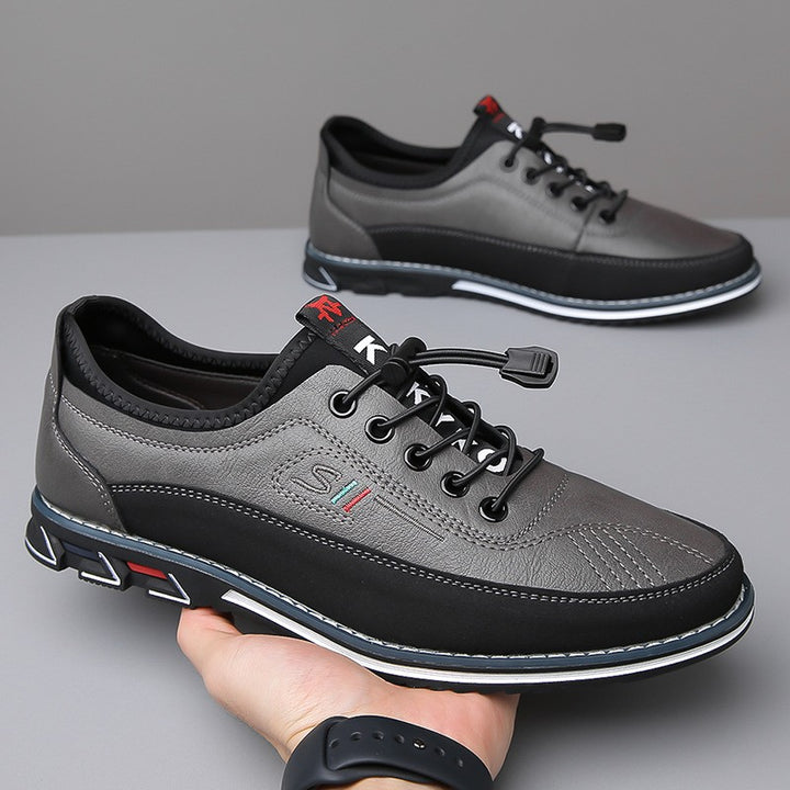 Main tenant une sneaker grise et noire, la seconde posée sur un socle blanc