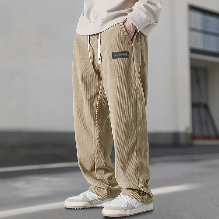 Pantalon en velours côtelé beige sable dans une rue, jambe large et cordon écru
