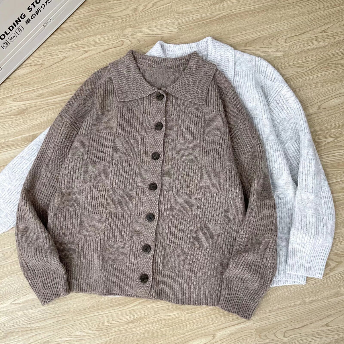 Cardigan en maille taupe à motif damier posé à plat sur un parquet clair