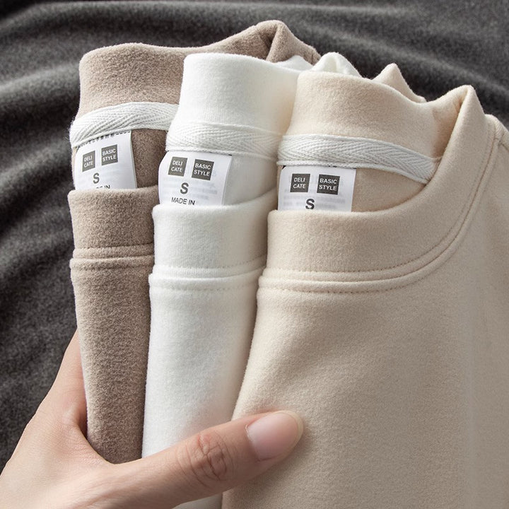 Main tenant trois sous-pulls thermiques pliés à intérieur polaire, coloris taupe, blanc et beige